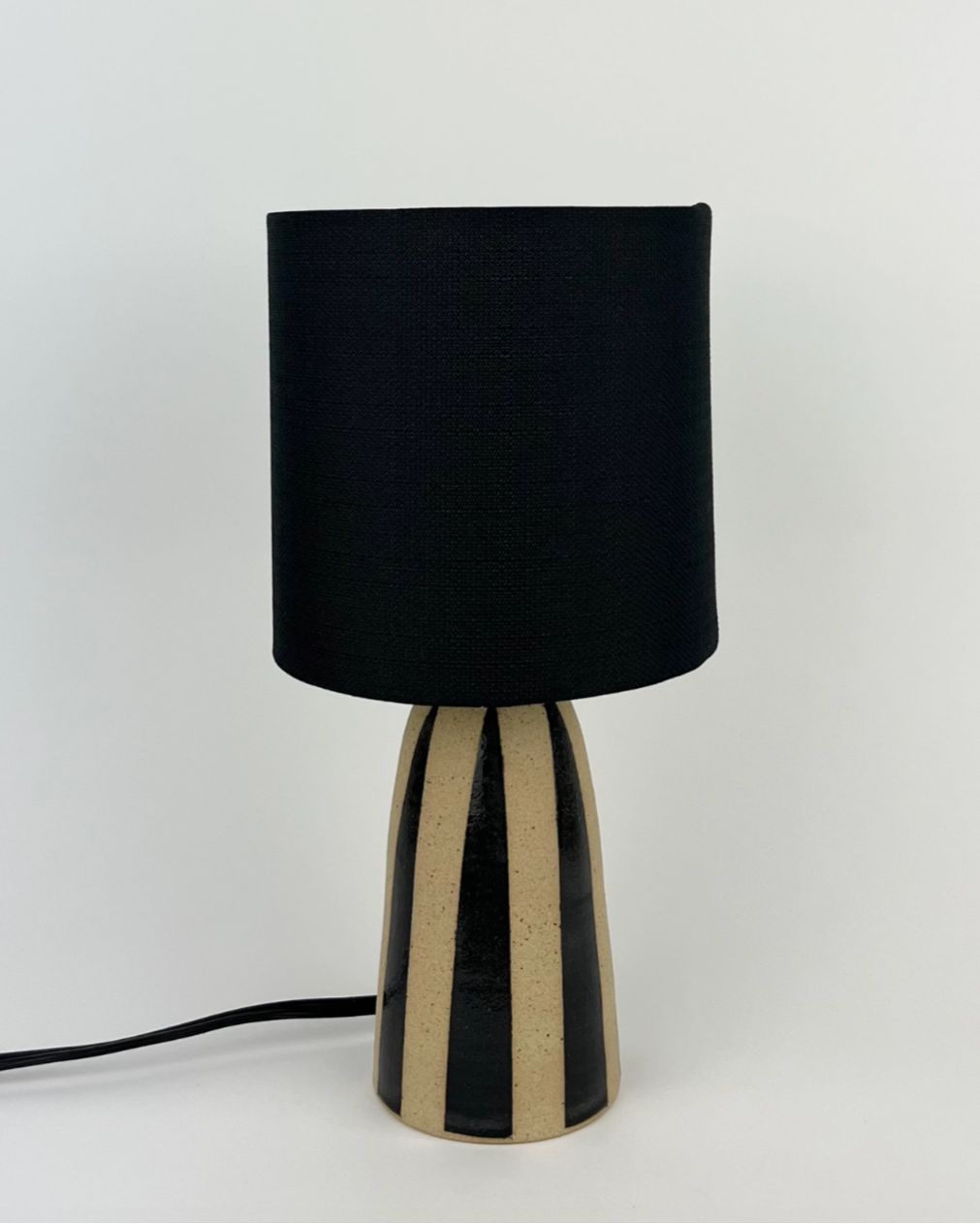 Handmade ceramic lamp with black stripes on a natural clay finish