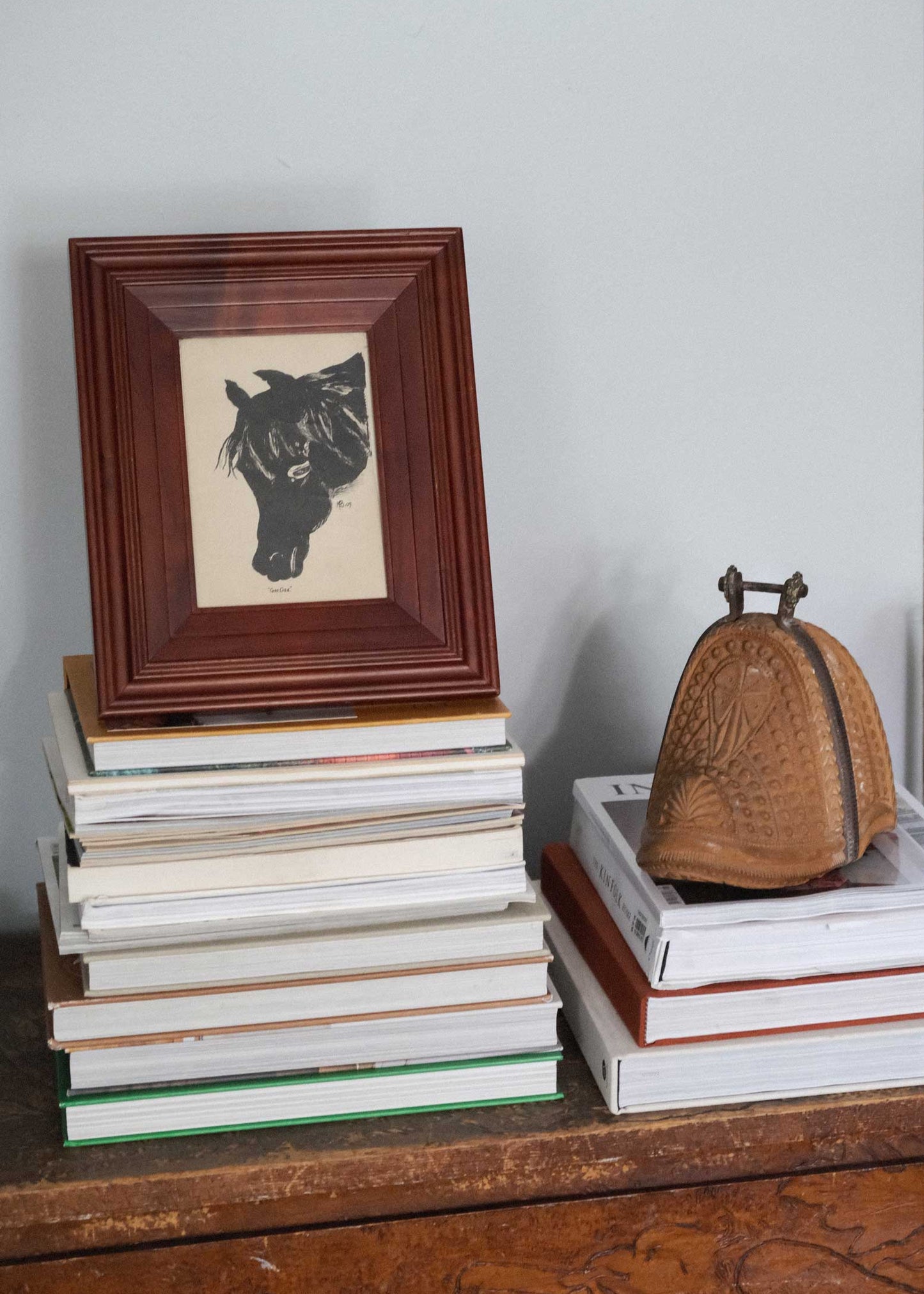 Stack of books with a framed picture and a decorative object on a wooden surface.