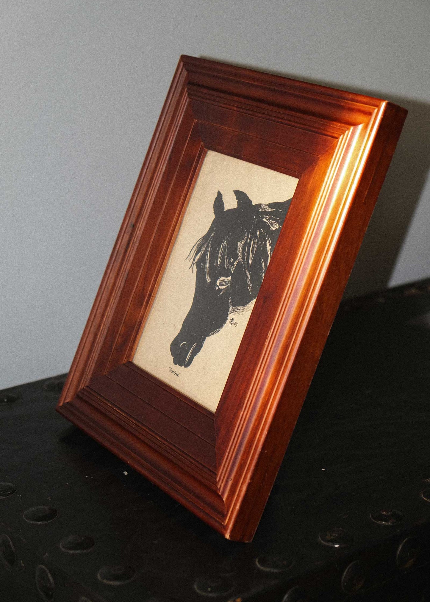 Wooden framed picture of a horse on a dark surface with a gray background