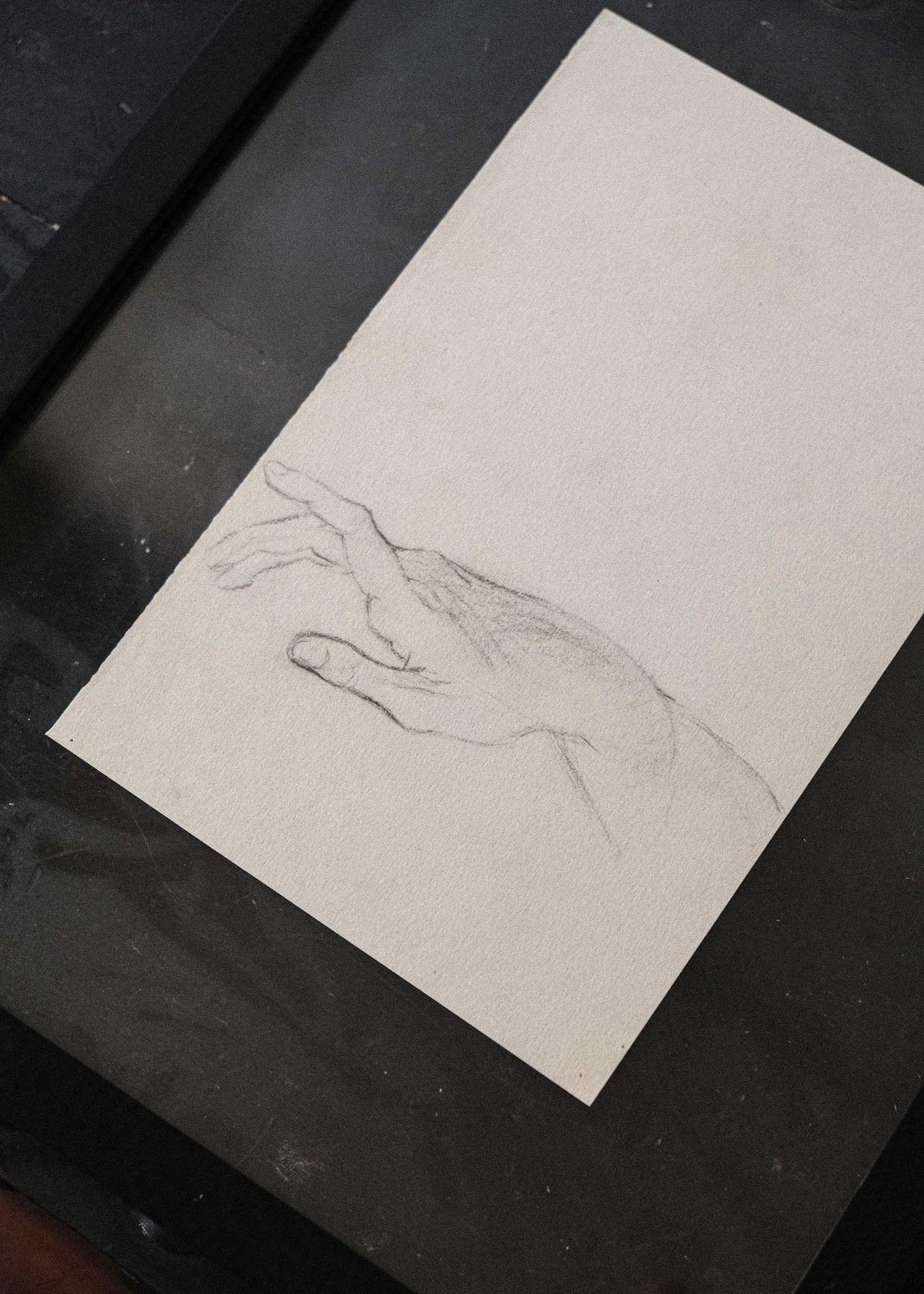 Pencil drawing of a hand on a piece of paper inside a black frame.