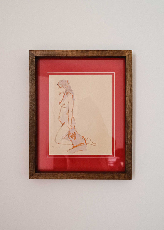 Framed artwork of a nude figure on a red background against a white wall