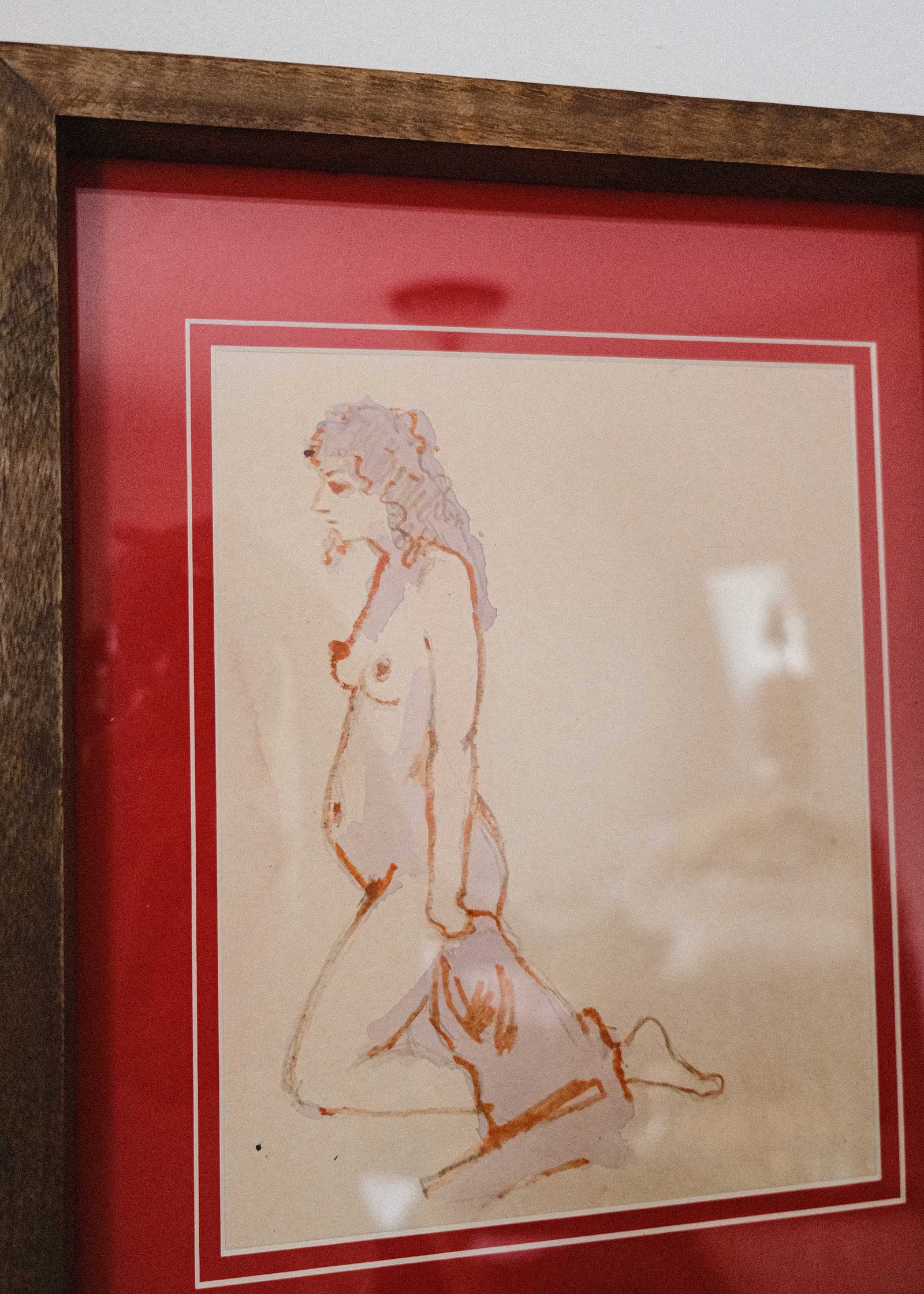 Framed artwork of a nude figure on beige paper with a red border.