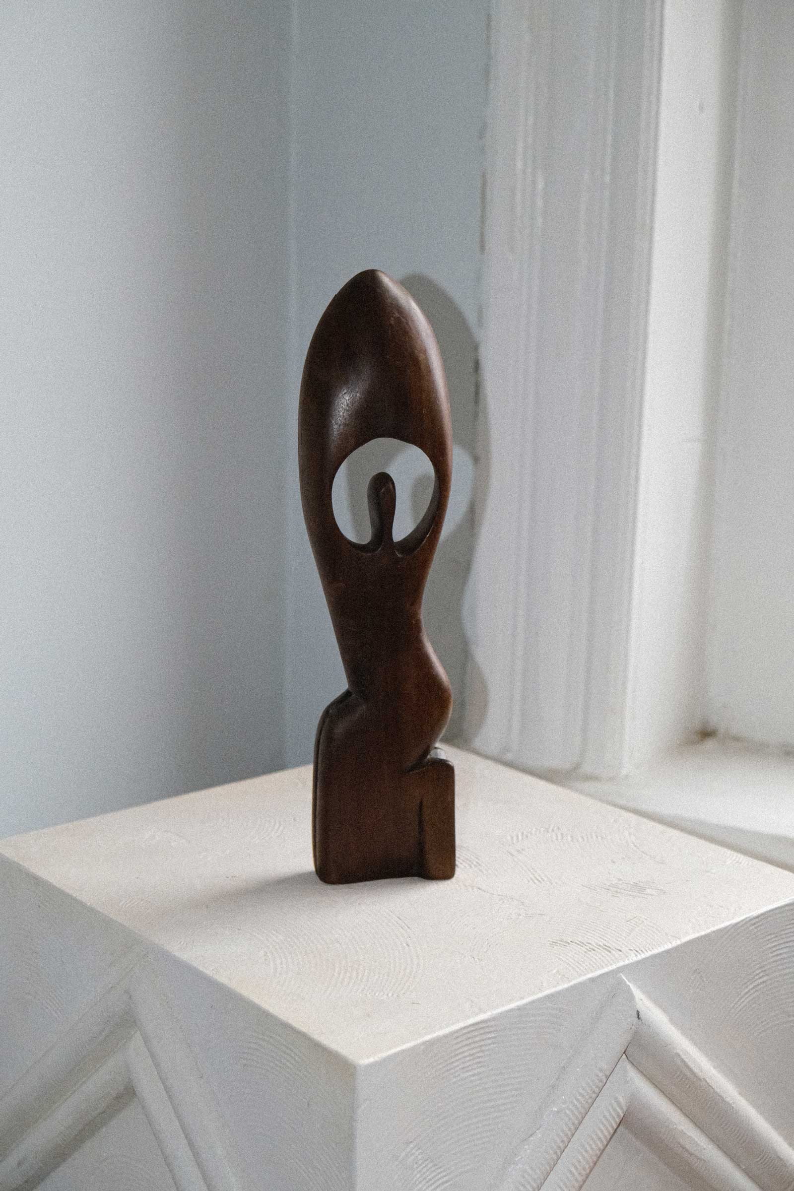 Wooden abstract sculpture on a white surface with a light gray wall background