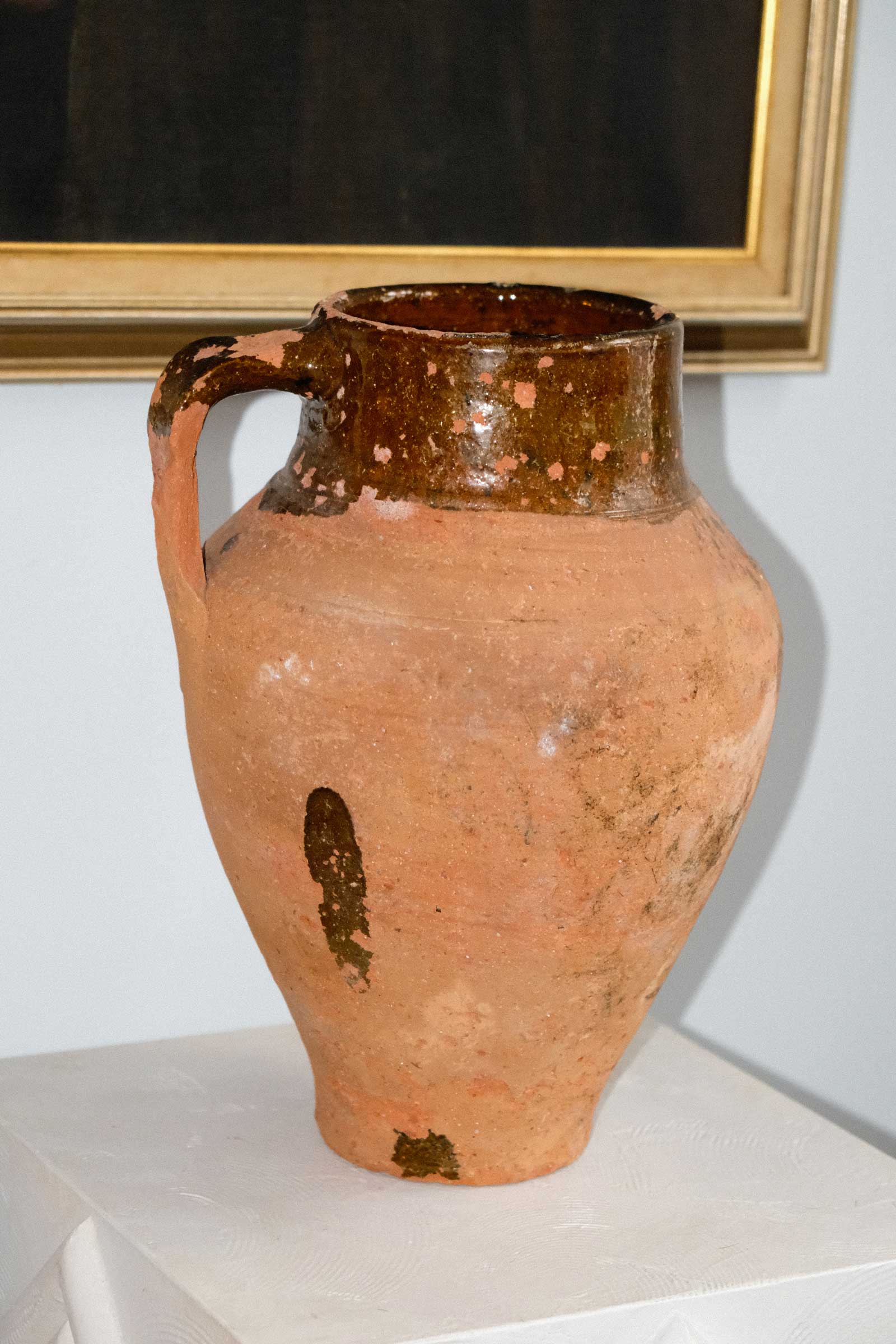 Terracotta vase with a glazed rim on a white surface against a light blue wall.