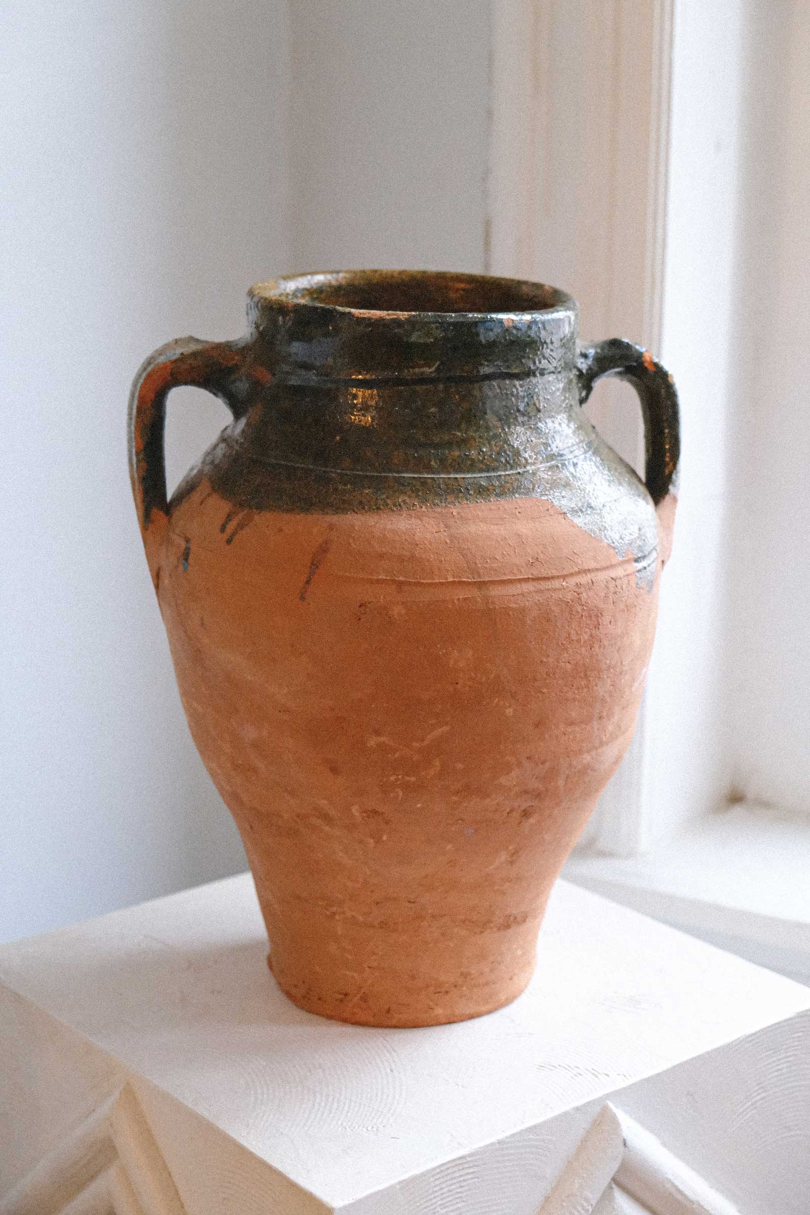 Terracotta vase with black handles on a white surface