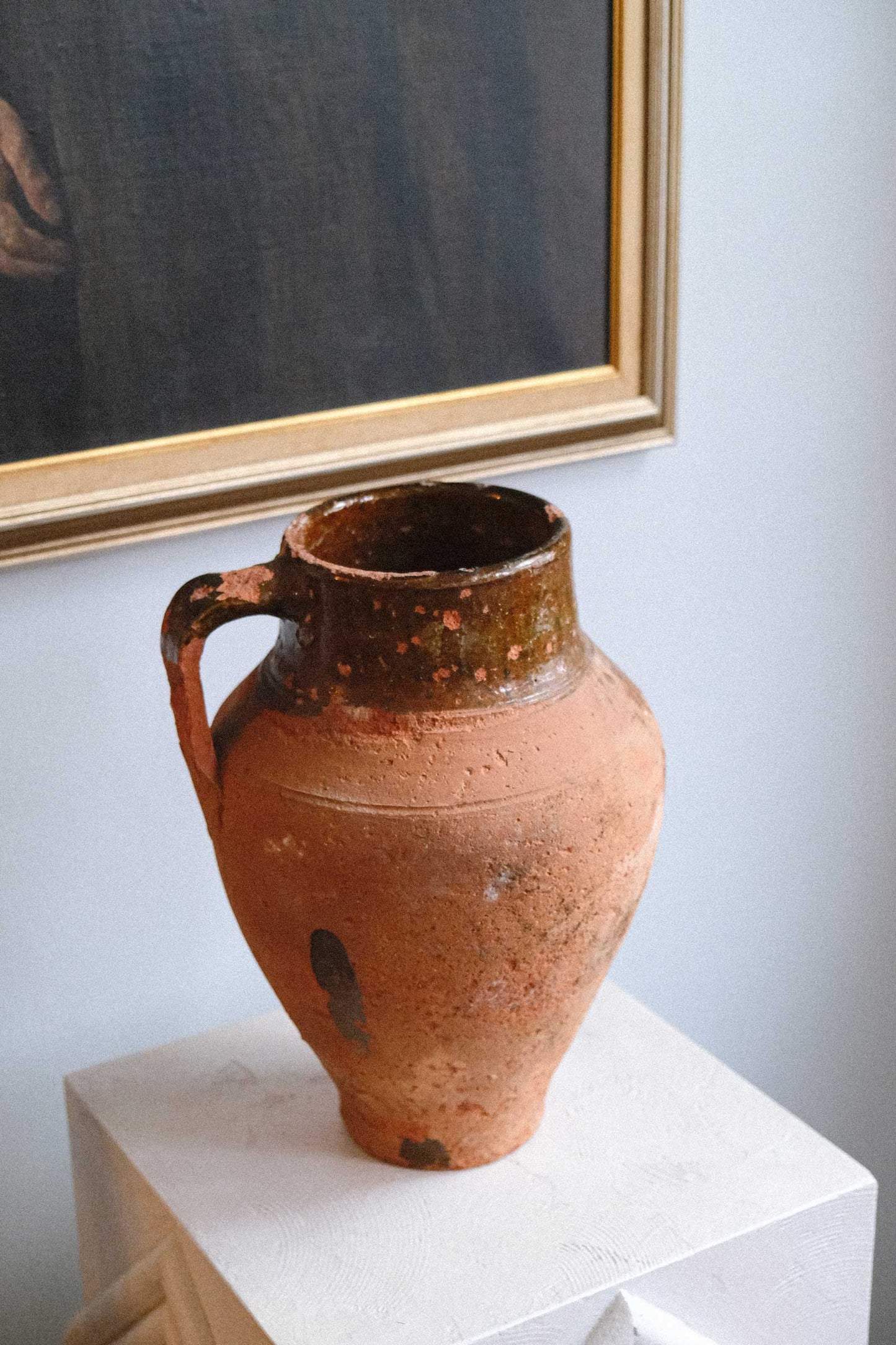 Brown ceramic vase on a white surface with a framed mirror in the background